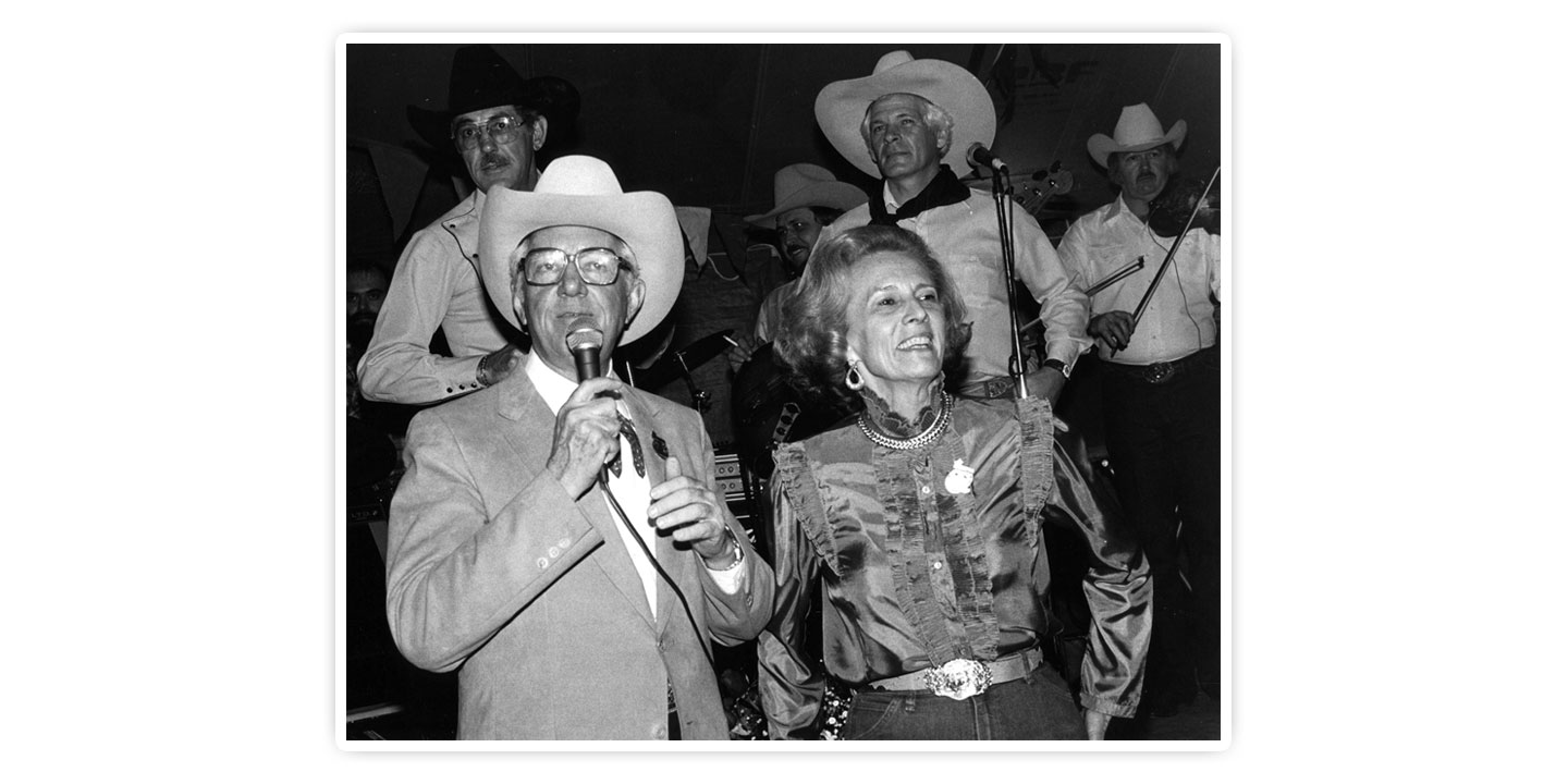 This is a black-and-white photo of Mr. John S. Justin, Jr. and Mrs. Jane Chilton Justin posing for a photo while Mr. Justin is speaking in a microphone.